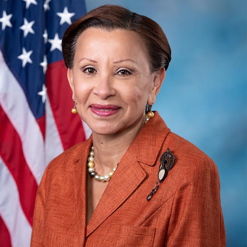 A person in orange suit with a flag behind her

Description automatically generated