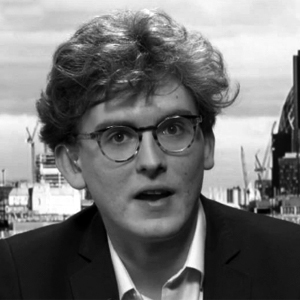 A person with glasses and a suit
Description automatically generated