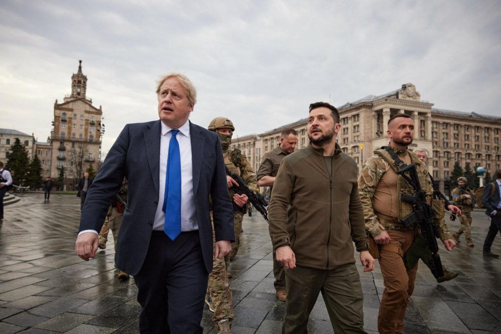 A person in a suit walking with soldiers in the background

Description automatically generated