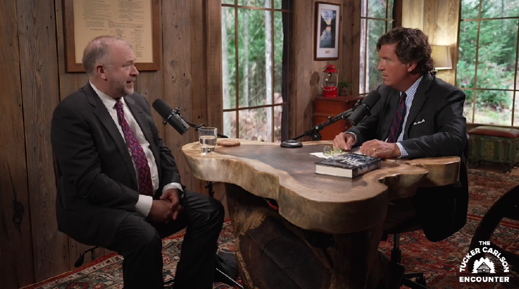 Two men in suits sitting at a table with microphones

Description automatically generated
