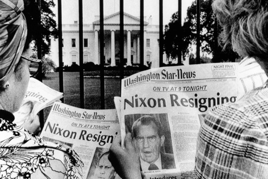 A group of people reading newspapers in front of a white house

Description automatically generated
