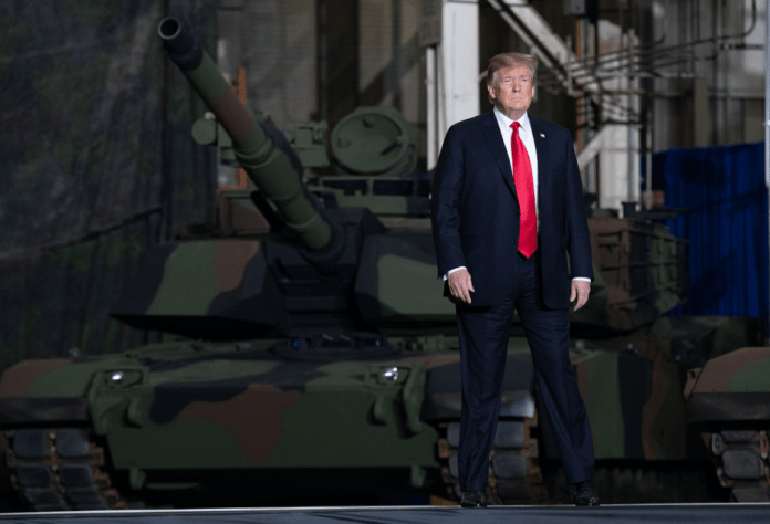A person in a suit and tie standing in front of a tank

Description automatically generated