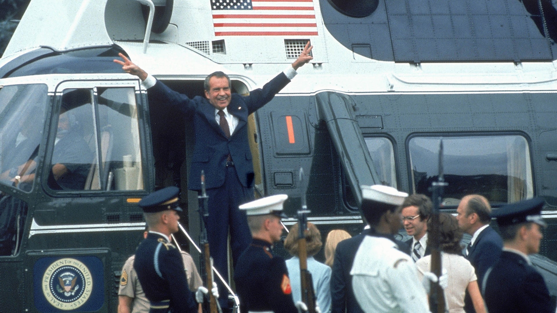 A person in a suit standing on a plane with his arms raised

Description automatically generated