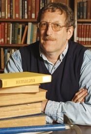 A person with a mustache and a stack of books
Description automatically generated