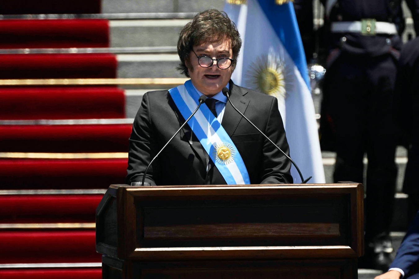 A person in a suit and tie standing at a podium

Description automatically generated