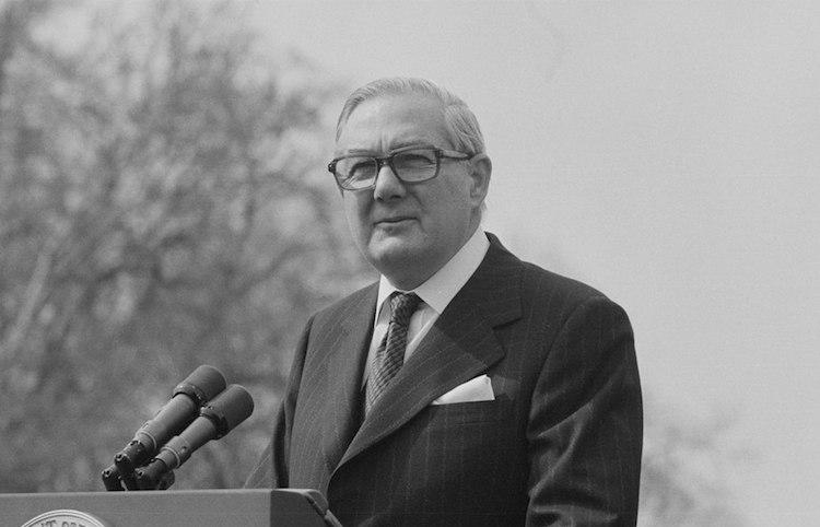 A person in a suit and tie standing at a podium Description automatically generated