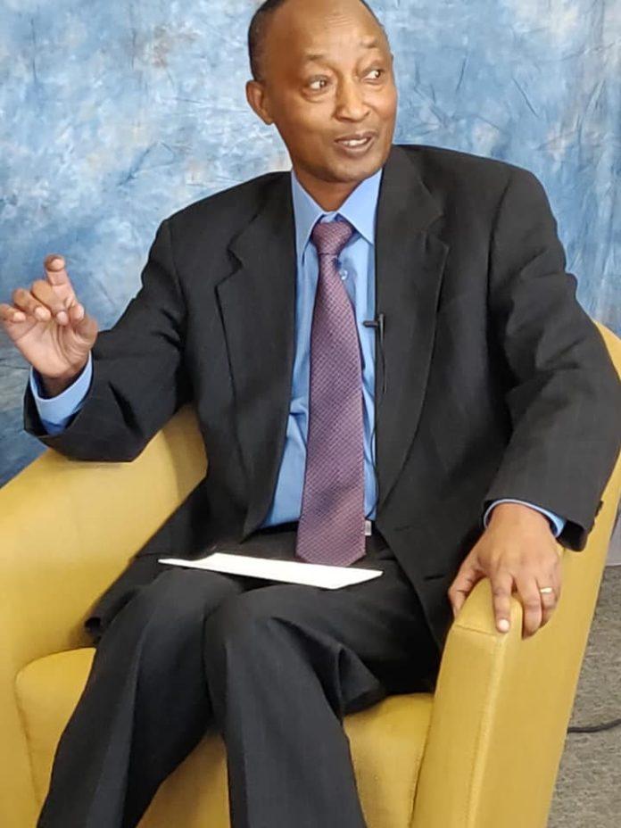 A person in a suit sitting in a yellow chair

Description automatically generated