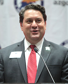 A person in a suit speaking into a microphone

Description automatically generated