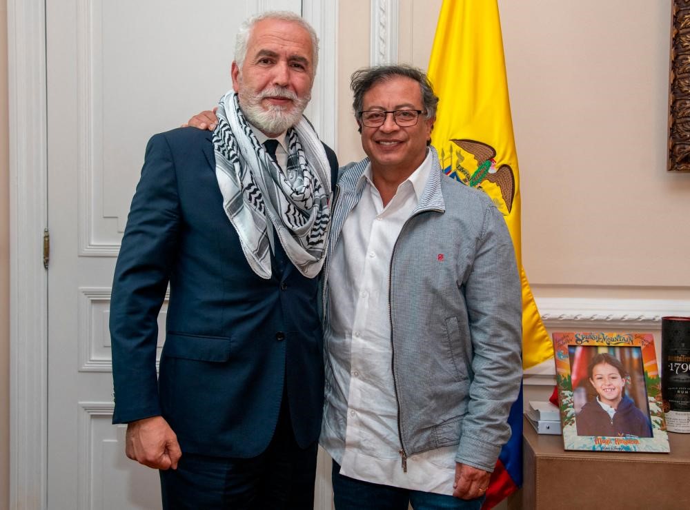 Two men standing together in front of a flag

Description automatically generated