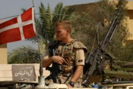 A person in uniform holding a rifle and a flag

Description automatically generated