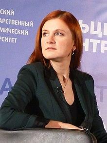A person with red hair sitting in front of a sign
Description automatically generated