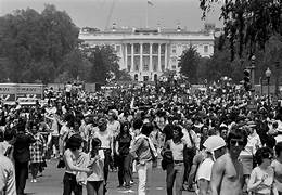 A crowd of people walking in front of a white house

Description automatically generated