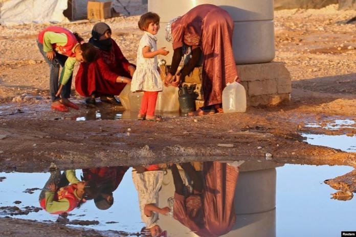 A group of people standing near a water well Description automatically generated
