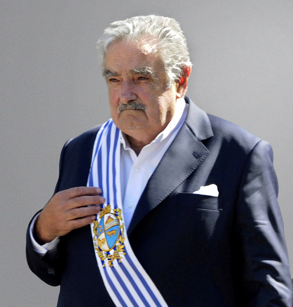 A person in a suit with a blue and white sash

Description automatically generated