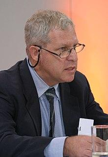 A person wearing glasses and a suit

Description automatically generated