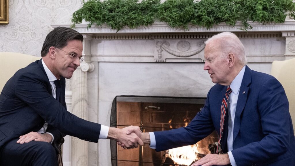 Two men shaking hands in front of a fireplace Description automatically generated