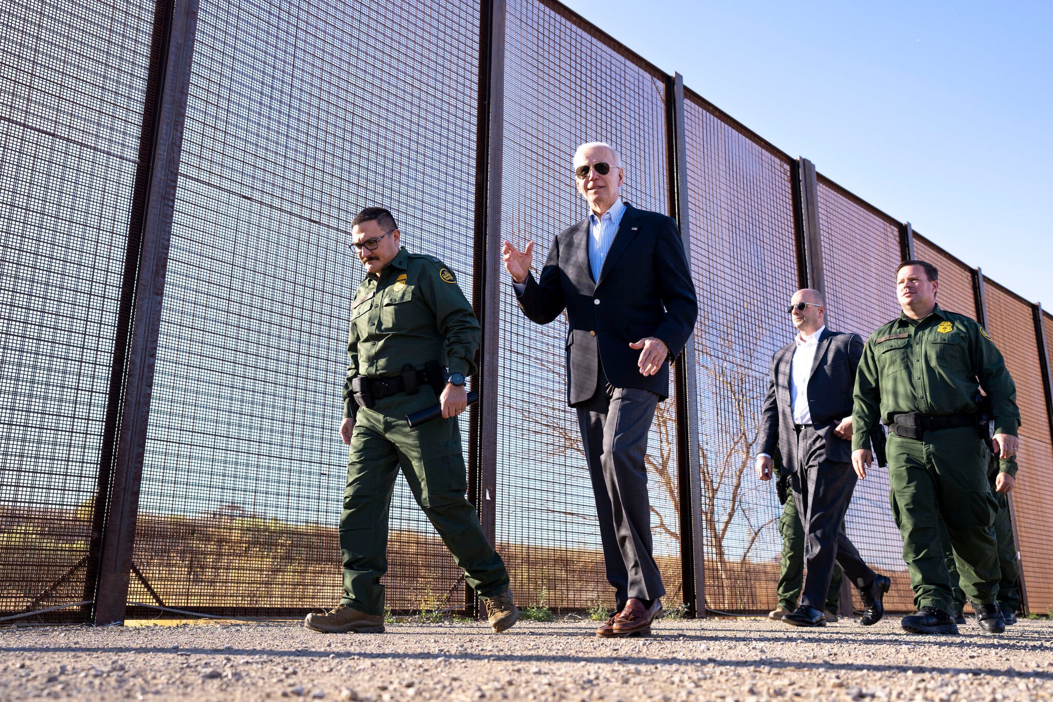 A group of men walking next to a fence
Description automatically generated