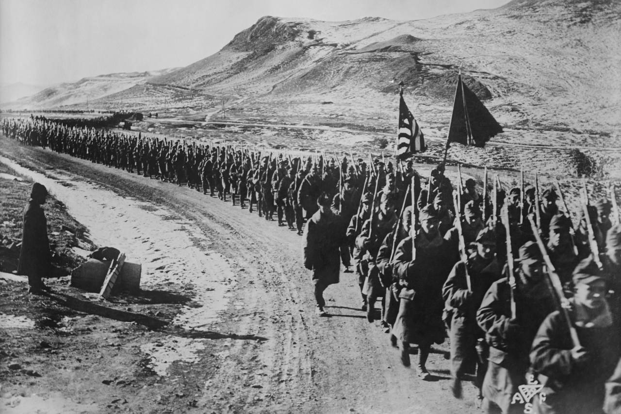 A group of soldiers marching on a dirt road
Description automatically generated