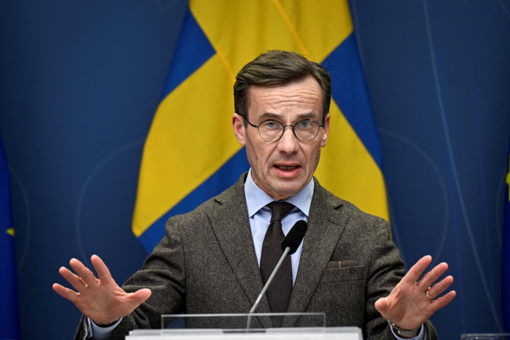 A person in a suit and tie speaking at a podium

Description automatically generated