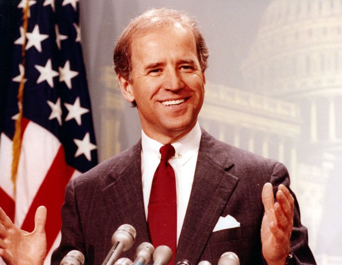 A person in a suit and tie standing in front of microphones

Description automatically generated