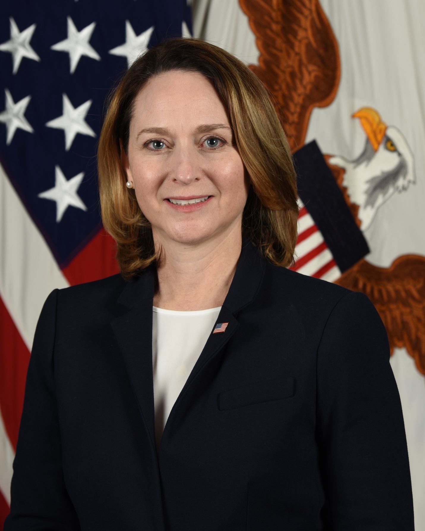 A person in a suit standing in front of a flag
Description automatically generated