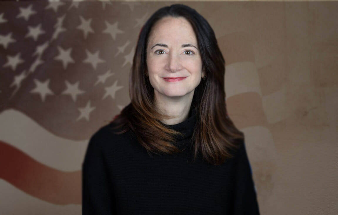 A person smiling in front of a flag
Description automatically generated
