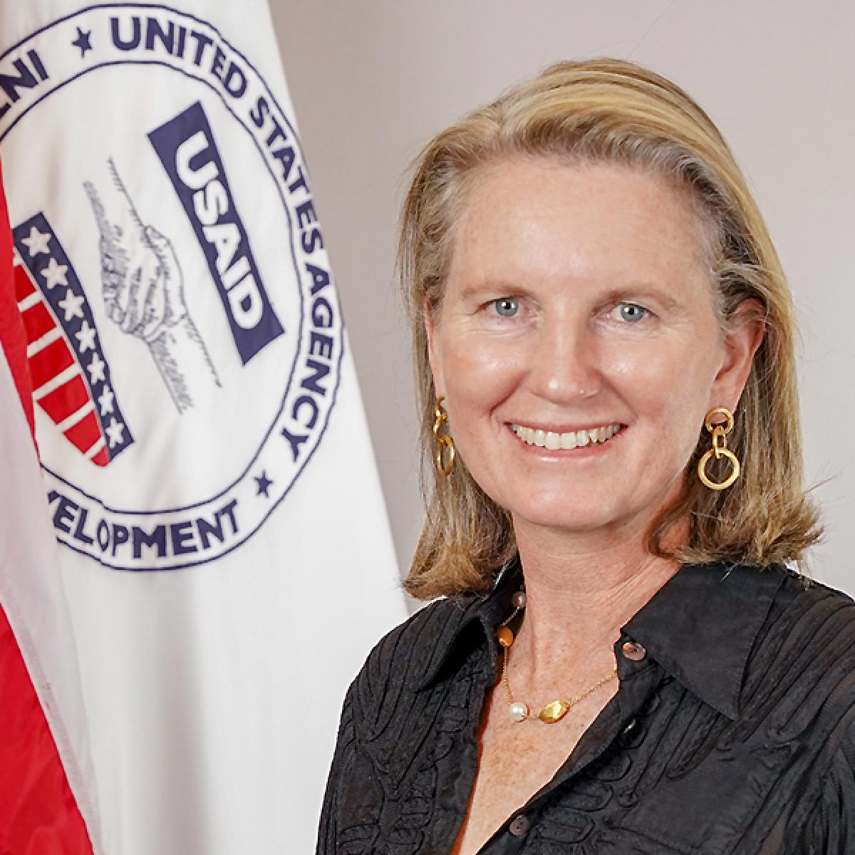 A person smiling in front of a flag
Description automatically generated