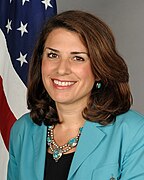 A person smiling in front of a flag
Description automatically generated