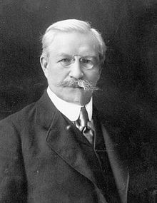A person with a mustache wearing a suit and tie
Description automatically generated