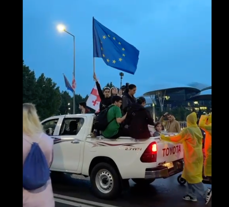 A group of people in a truck with a flag

Description automatically generated