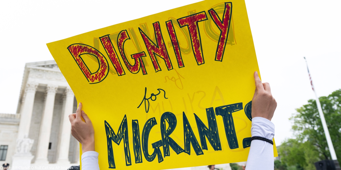 A person holding a yellow sign
Description automatically generated