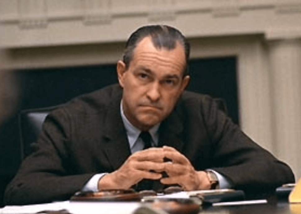 A person in a suit sitting at a table
Description automatically generated