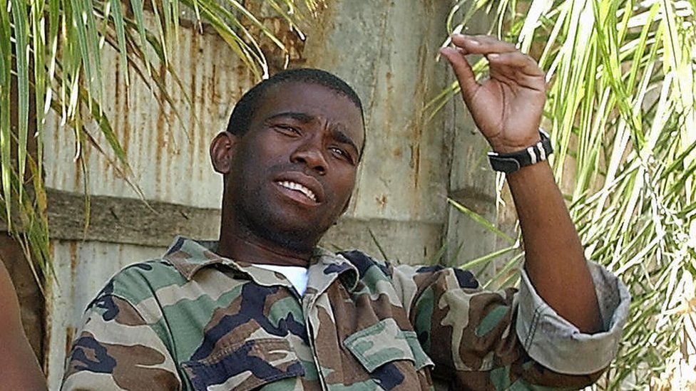A person in camouflage jacket holding a cigarette

Description automatically generated