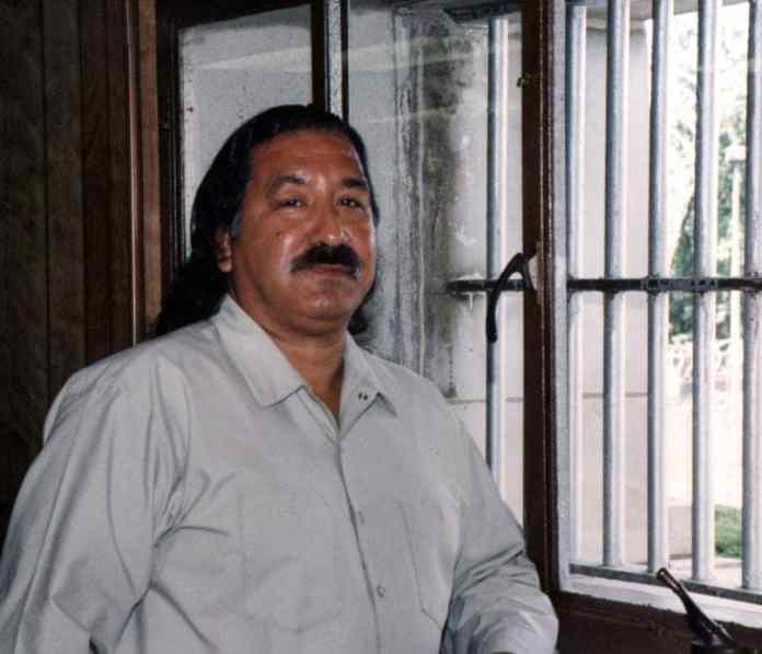 A person with a mustache sitting in front of a window Description automatically generated