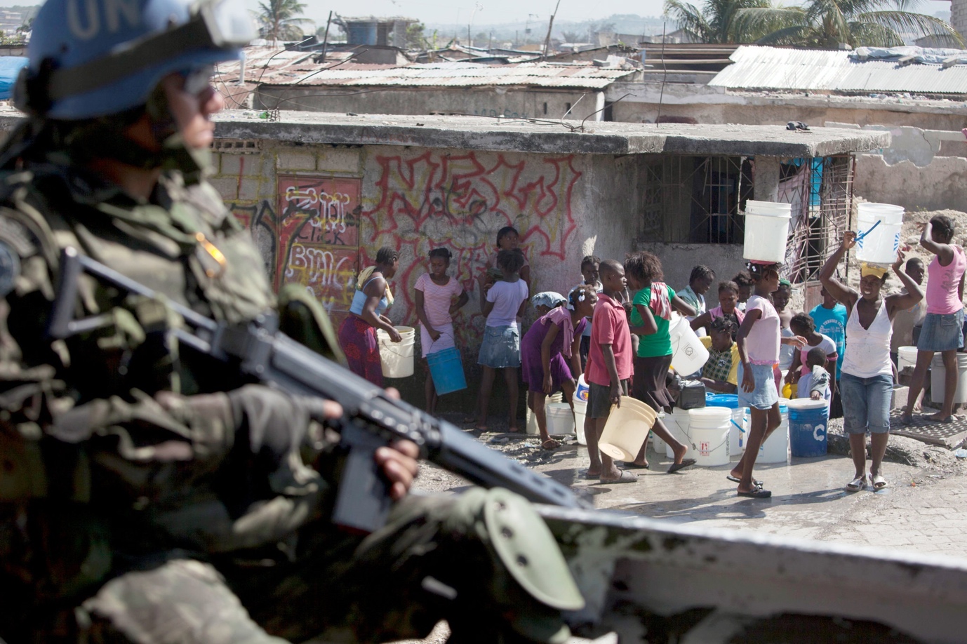 A soldier holding an object next to a group of people

Description automatically generated