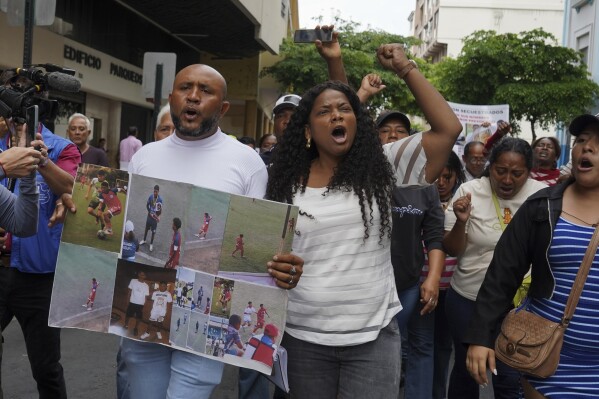 Luis Arroyo, left, carries photos of his two missing sons, Ismael and Josué, who were last seen on Dec. 8 running away from a military convoy with two other youths, as he protests with his family and activists outside the prosecutor's office in Guayaquil, Monday, Dec. 23, 2024. (AP Photo/Cesar Munoz)