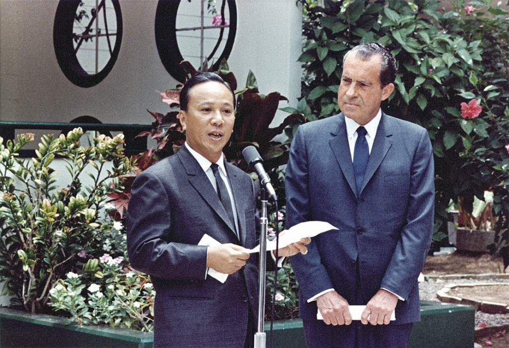 A person in a suit giving a speech to another person

Description automatically generated