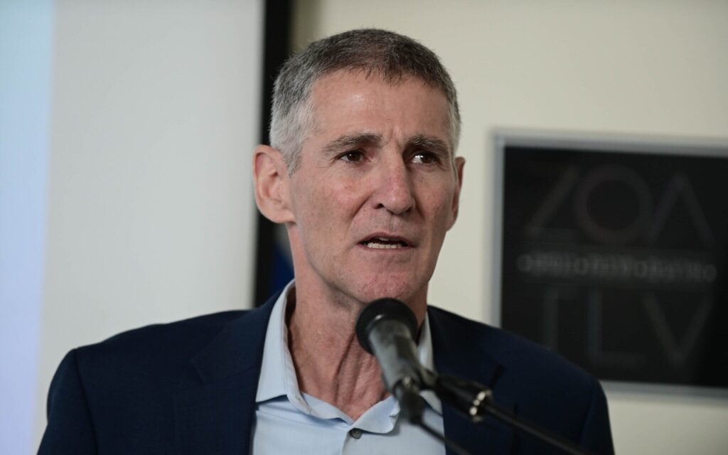 A person in a suit speaking into a microphone Description automatically generated