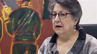 A person in glasses with a painting behind her

Description automatically generated