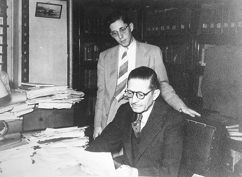 A person in suit and tie looking at papers

Description automatically generated