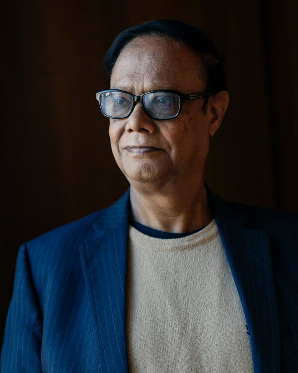 Ahsan Mansur, wearing glasses and a striped navy blazer, stands looking off into the distance.