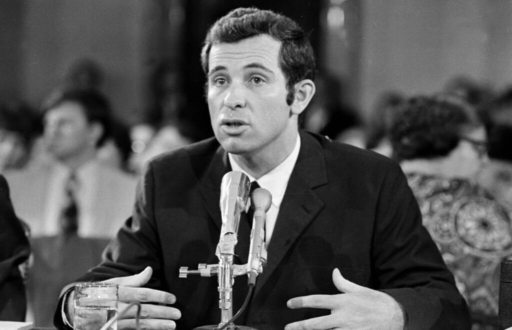 A person in a suit speaking into a microphone

Description automatically generated