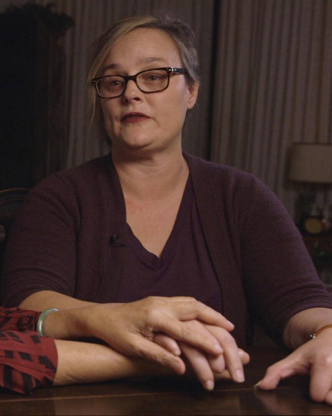 A person sitting at a table with her hands folded

Description automatically generated
