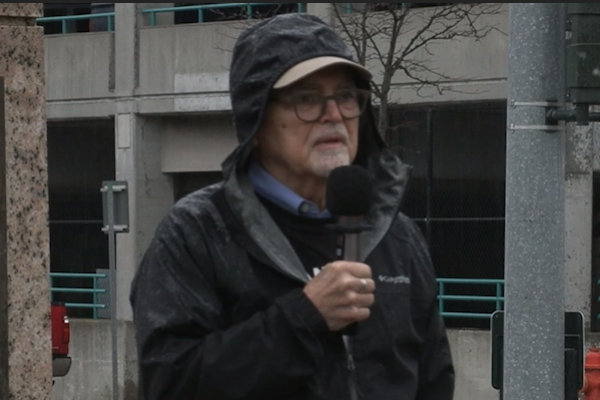 A person wearing a raincoat and holding a microphone
AI-generated content may be incorrect.