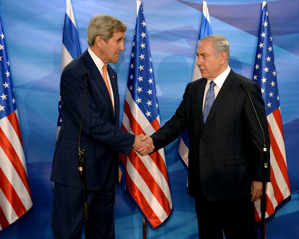 A couple of men shaking hands in front of flags

Description automatically generated