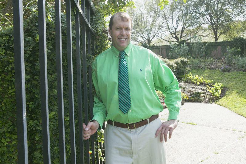 A person in a green shirt and tie leaning against a fence

Description automatically generated