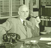 A person sitting at a desk holding a pipe
Description automatically generated