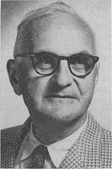 A person wearing glasses and a checkered suit
Description automatically generated
