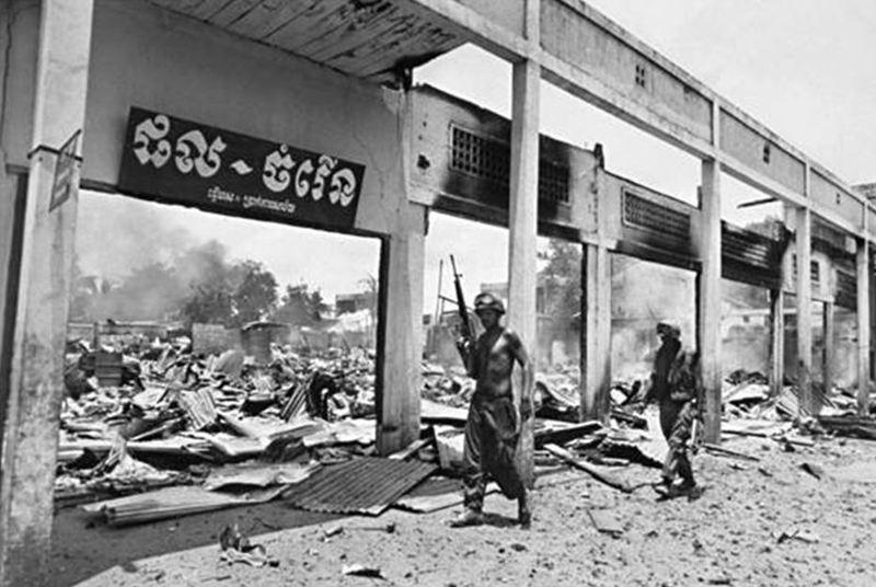 Men holding guns in front of a destroyed building
Description automatically generated