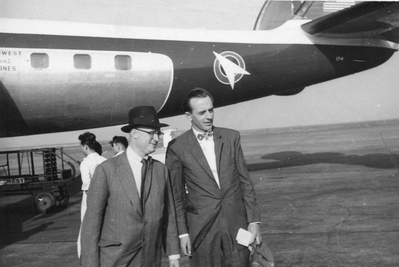 A couple of men standing in front of an airplane
Description automatically generated